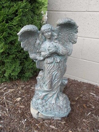 A statue of a woman with wings standing in front of a brick wall.