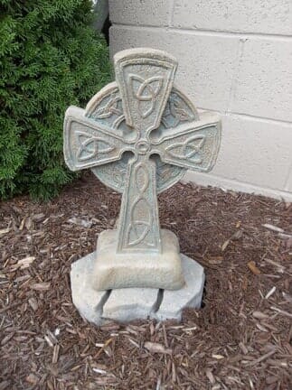 A stone cross is sitting on top of a pile of mulch in front of a brick wall.