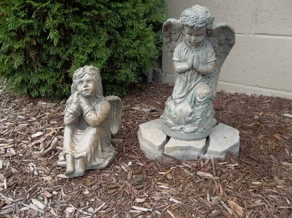 Two statues of angels are sitting on a pile of mulch.