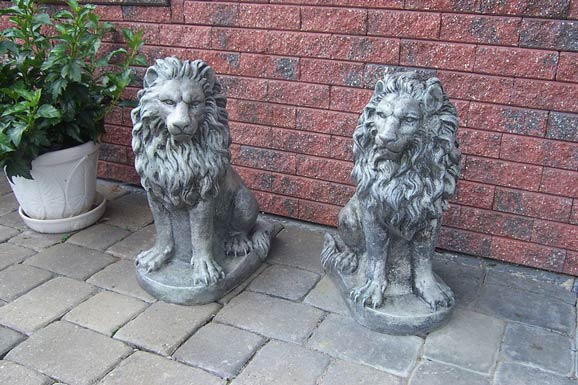 Two statues of lions are sitting on a brick sidewalk in front of a brick wall.