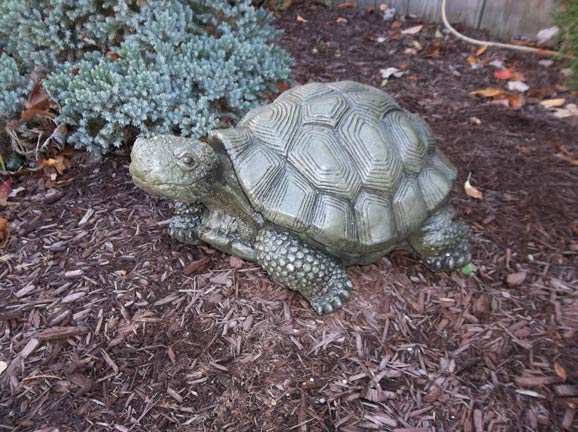 A statue of a turtle is sitting on a pile of mulch.
