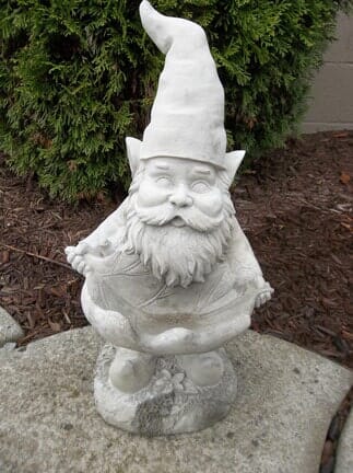 A statue of a gnome with a beard and hat is sitting on a rock.