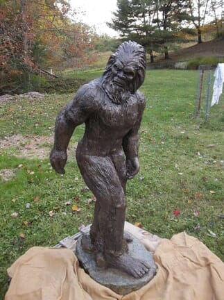 A statue of a man with a beard is standing in the grass.