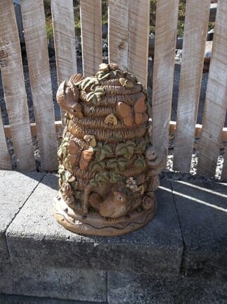 A statue of a beehive is sitting next to a wooden fence.