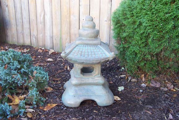 A small stone lantern is sitting in the dirt in front of a wooden fence.