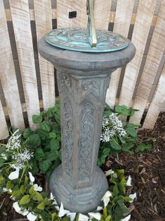 A sundial is sitting in a garden next to a wooden fence.