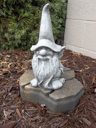 A statue of a gnome with a beard and hat is sitting on a rock.
