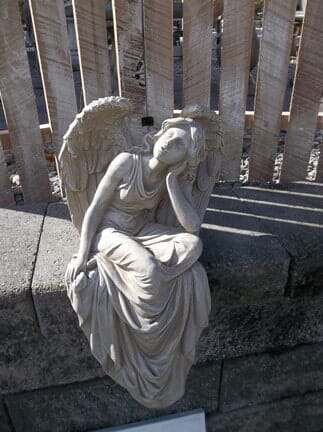 A statue of an angel sitting on a wall next to a wooden fence.