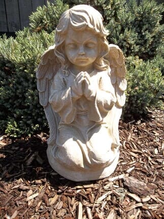 A statue of a praying angel is sitting on a pile of mulch.