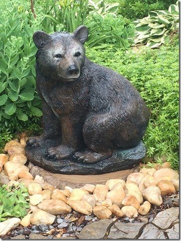 A statue of a bear sitting on a rock in a garden.