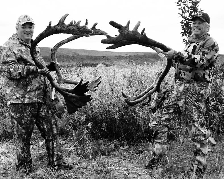 Two men are holding large antlers in a field.