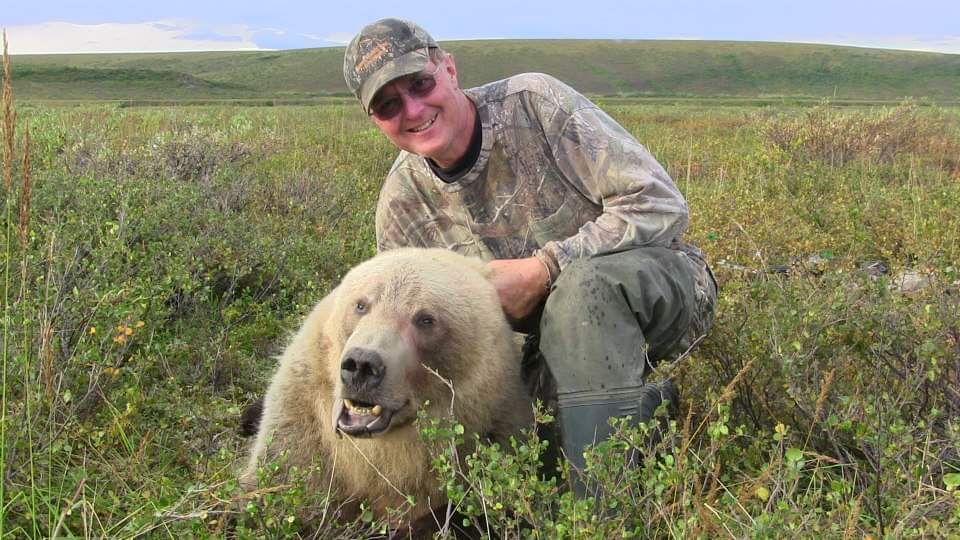 A man is kneeling down next to a polar bear in a field.