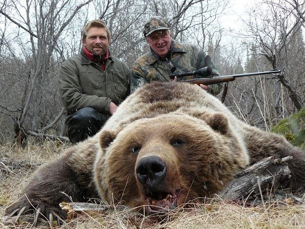 Two men are standing next to a large brown bear.