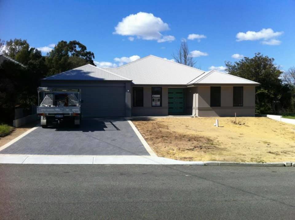 Suburban house with a white roof, blue car in the driveway, and dry front lawn under a bright sky.
