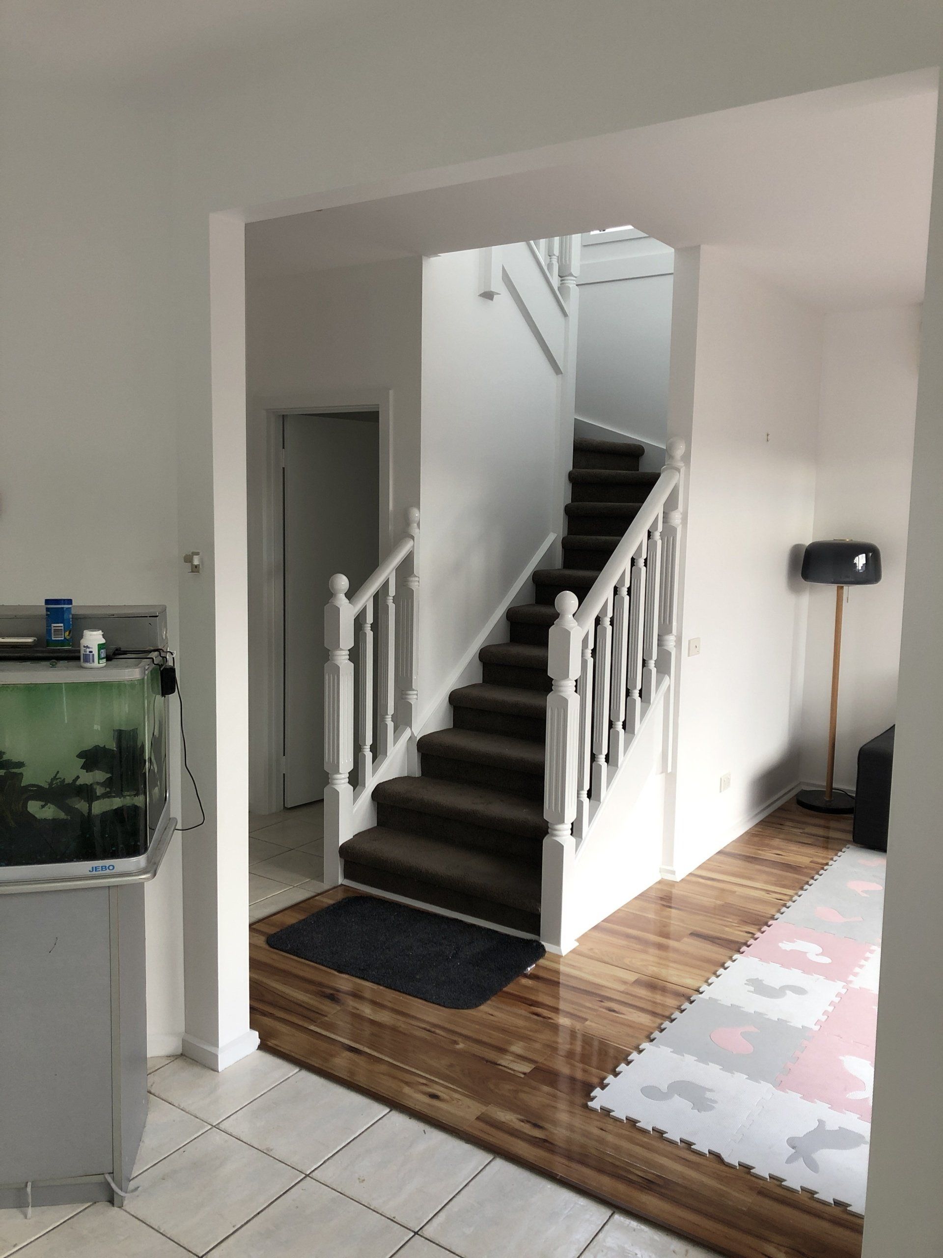 Interior hallway with carpeted staircase, white railings, and tiled floor by a fish tank and rug.