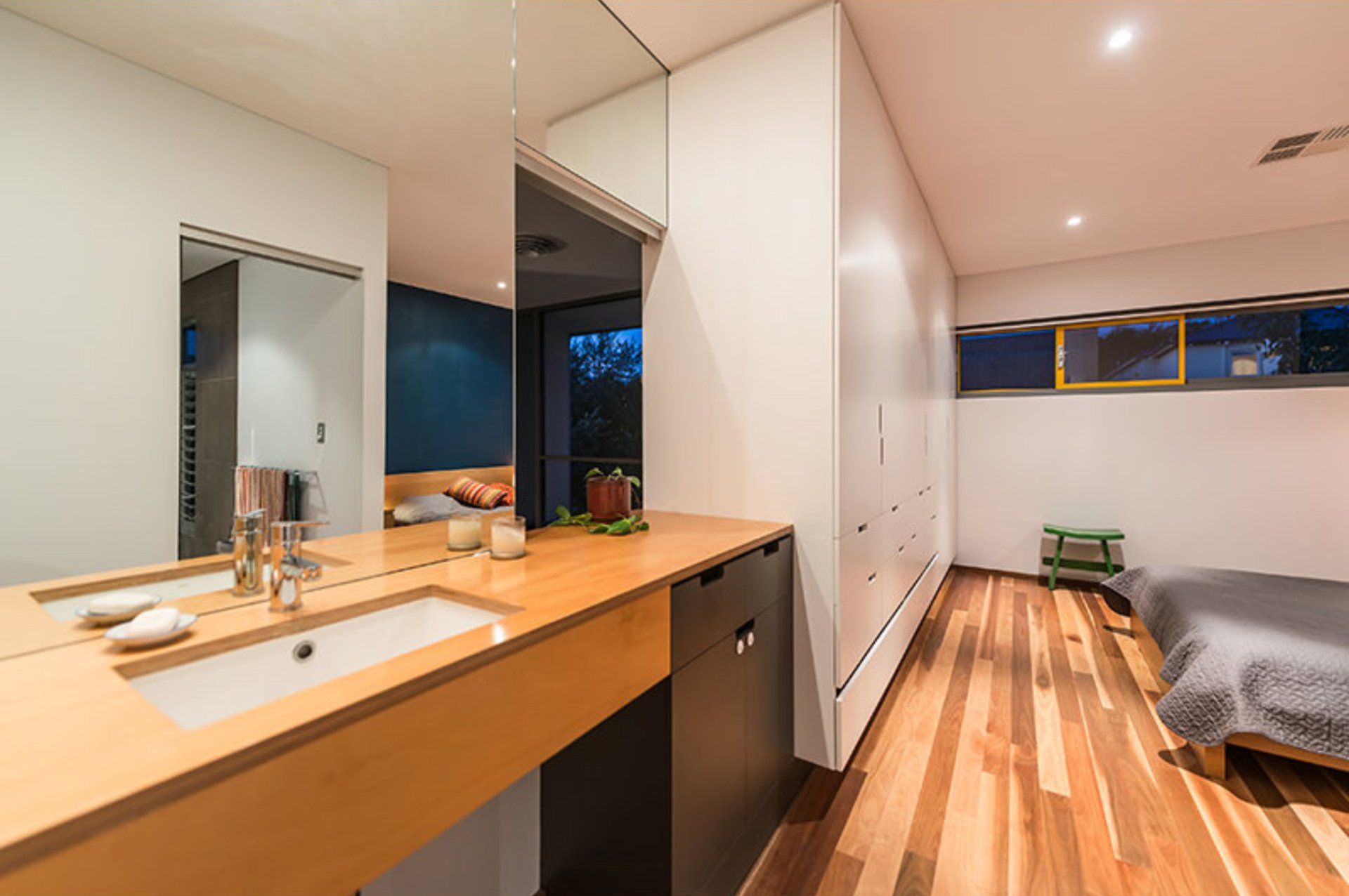 Modern bedroom with wooden floors, mirror vanity, bed, and large window at night