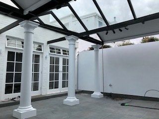 Patio with white columns, black pergola beams, French doors, and white privacy walls under construction