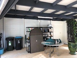 Covered patio with storage shelves, trash bins, folding table, and potted plant