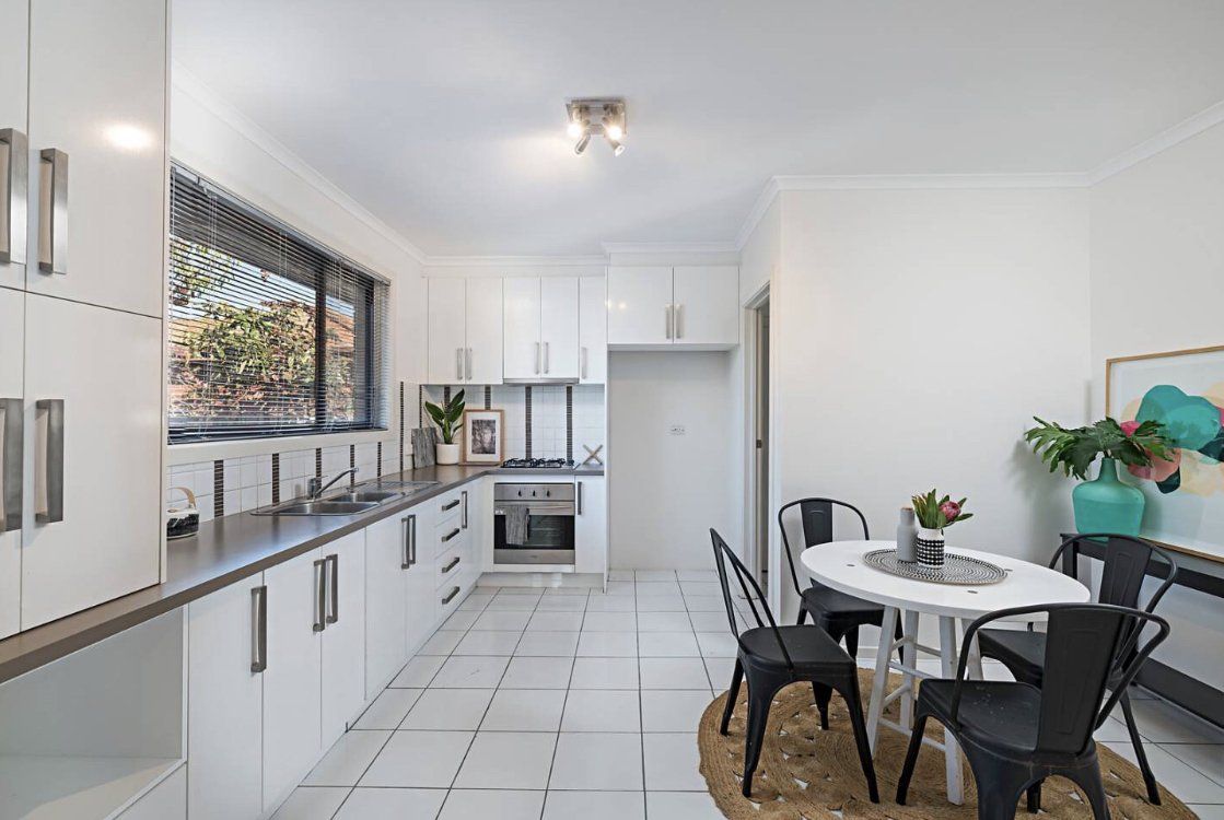 Bright modern kitchen with white cabinets, black countertops, and a small round dining table by the window.