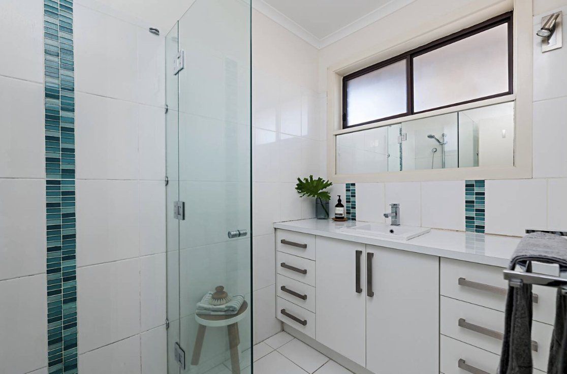 Modern white bathroom with glass shower, vanity, mirror, and blue accent tiles