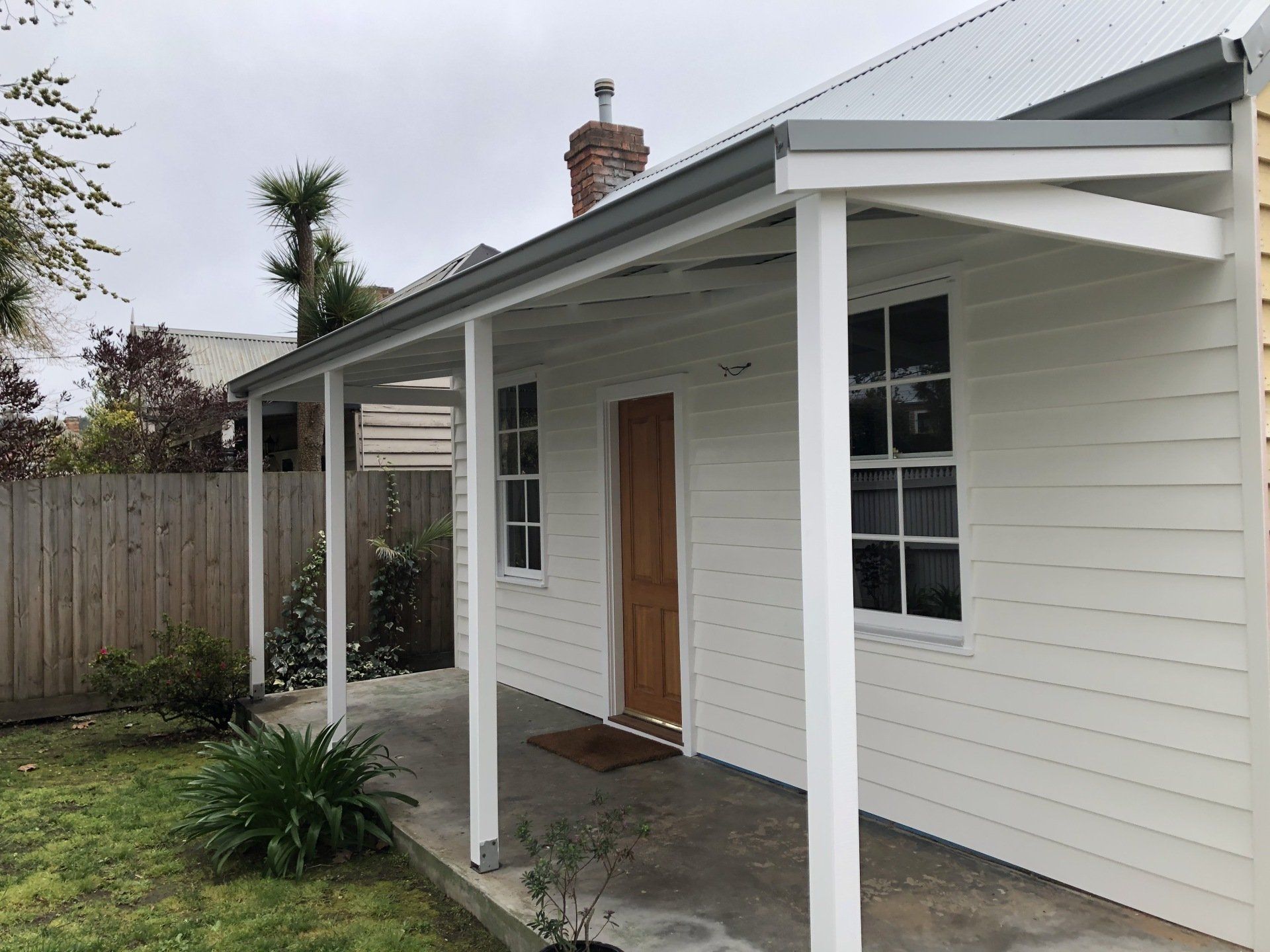 White house exterior with front porch, wood door, and metal roof