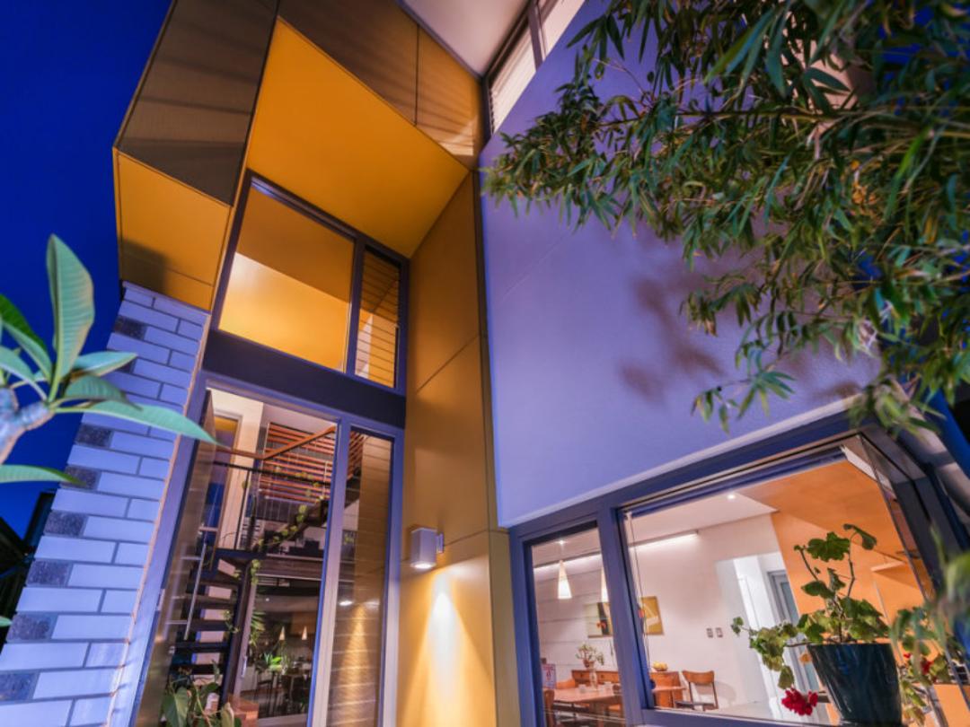 Modern house exterior at dusk with warm interior lights and tall windows