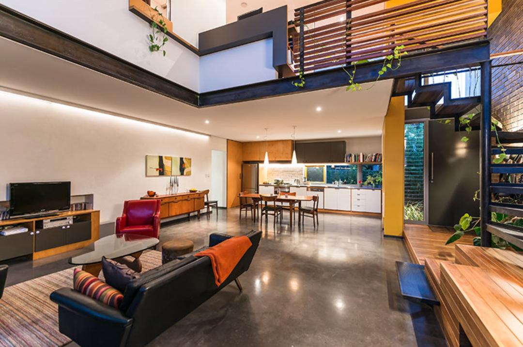 Modern loft living room with black sofa, dining area, kitchen, and mezzanine staircase