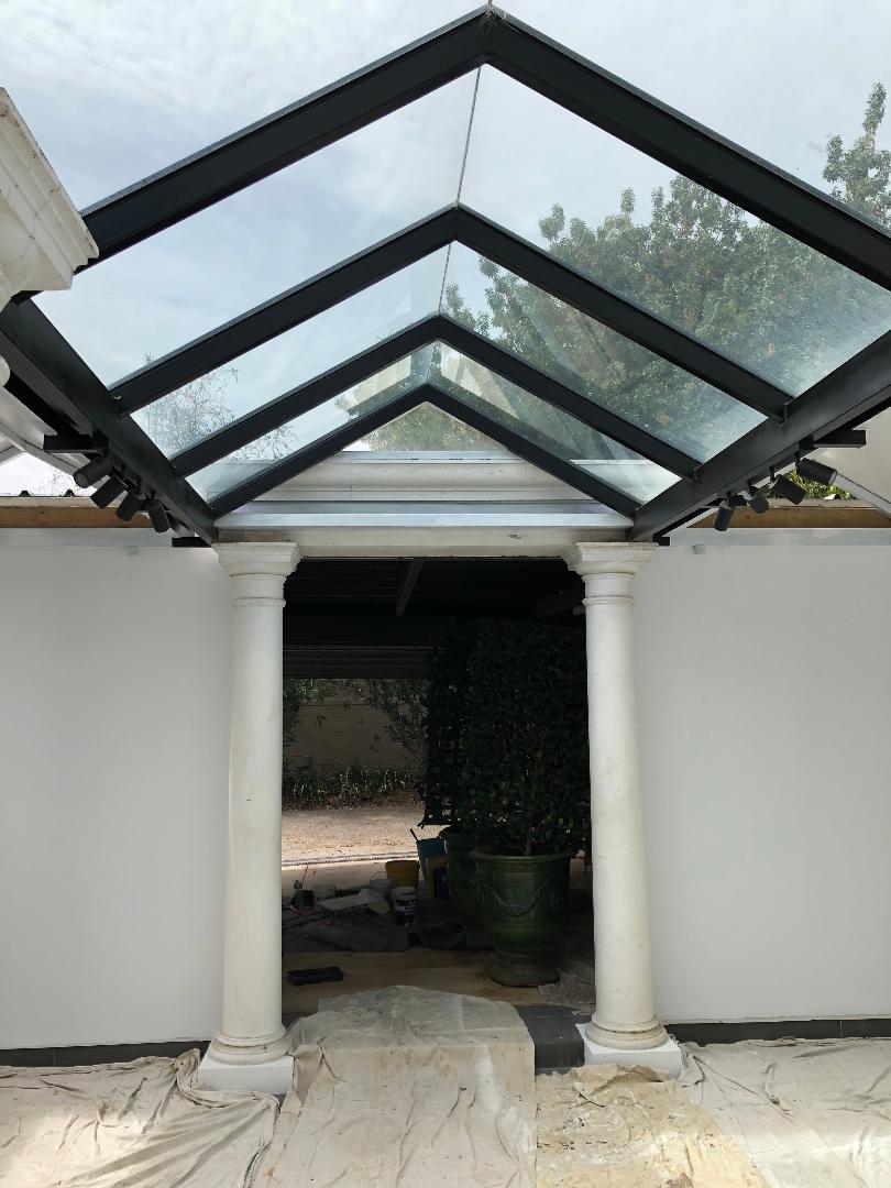 Glass-roofed patio or entryway with white walls and columns, viewed from the front.
