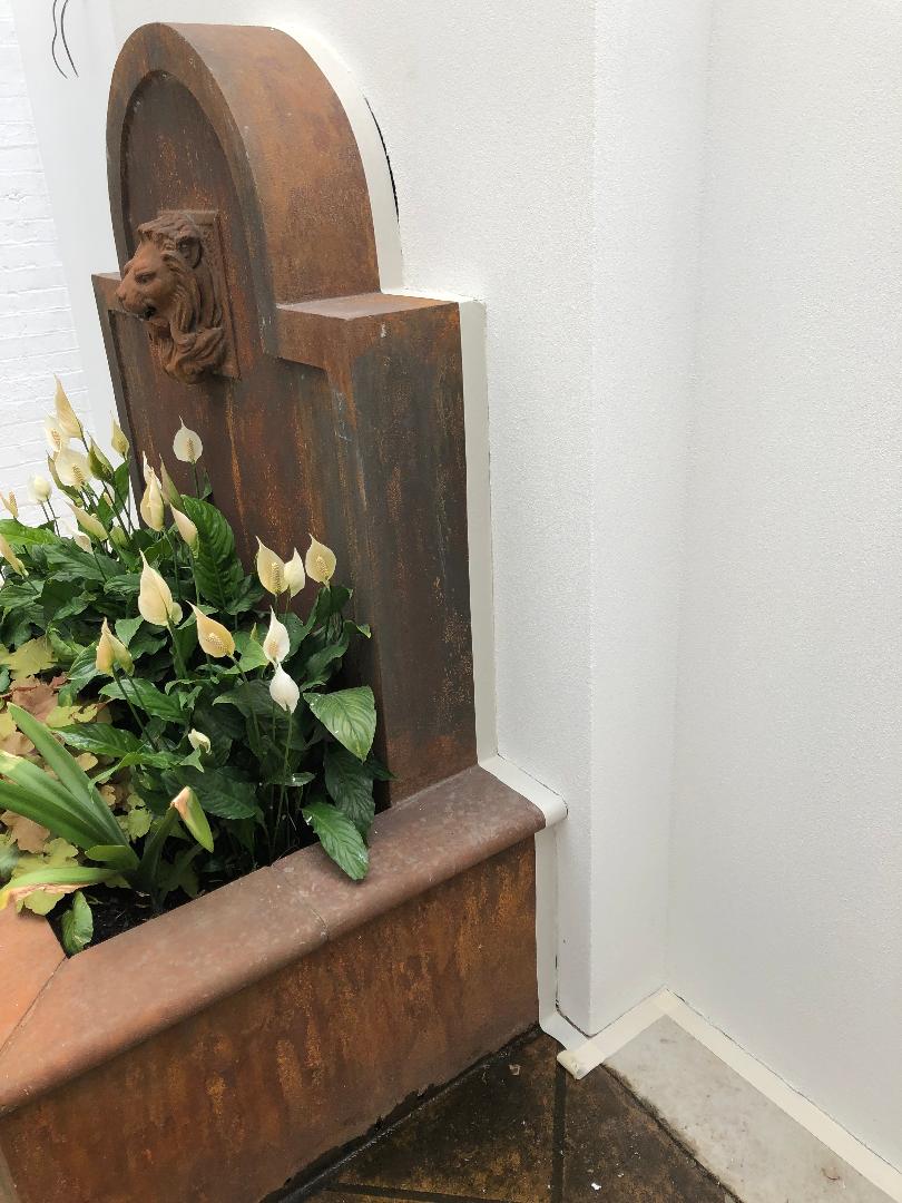 Rustic wooden fountain with white flowers beside a white wall on a tiled floor
