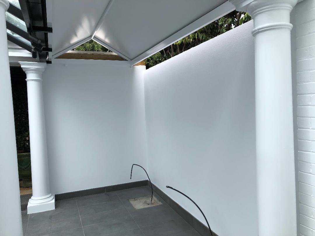 Covered outdoor walkway with white walls, columns, and curved black railings under a roof.