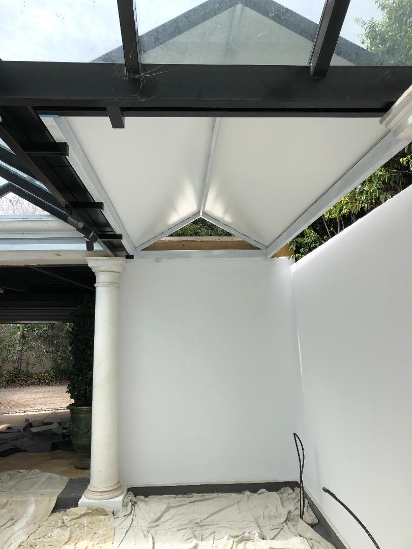 Covered patio with a white wall, column, and retractable shade sail under a glass roof.