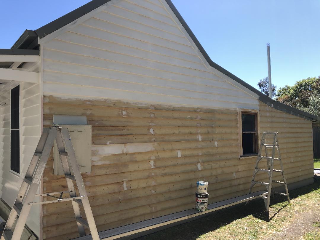 House exterior with beige siding being repaired, ladder and tools leaning against the wall