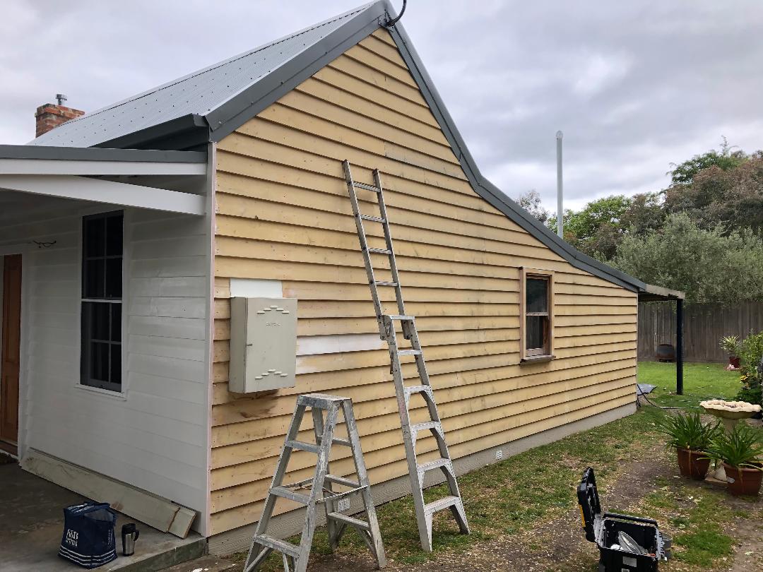 House exterior with beige siding and roof under repair, ladders leaning against the wall