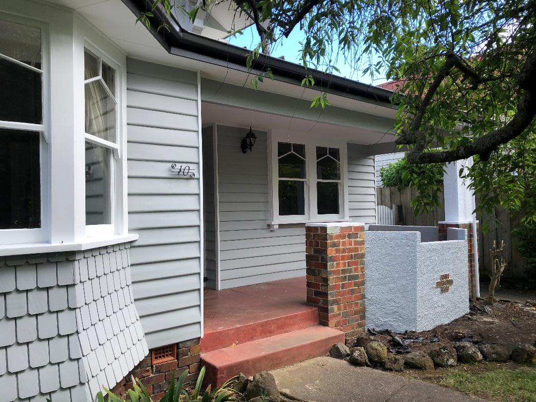 Front porch of a house with white siding, red steps, brick pillars, and a small front garden area
