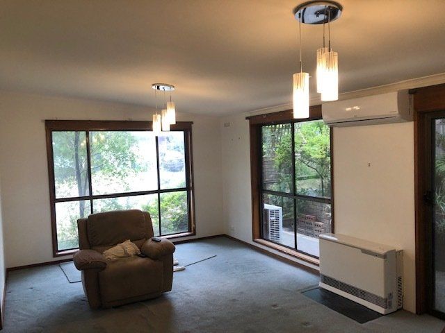 Empty living room with large windows, recliner, hanging lights, and wall-mounted heater.
