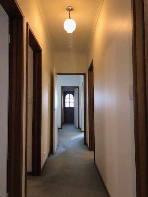 Narrow beige hallway with wooden doorways, ceiling light, and a window at the far end.
