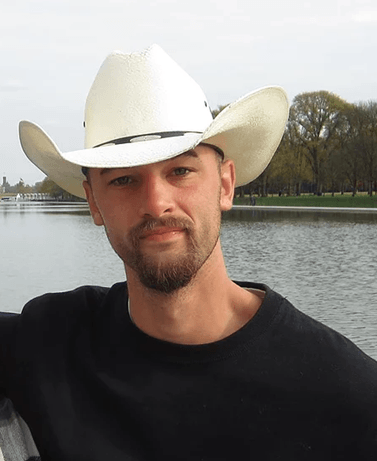 A man wearing a cowboy hat is standing in front of a body of water.