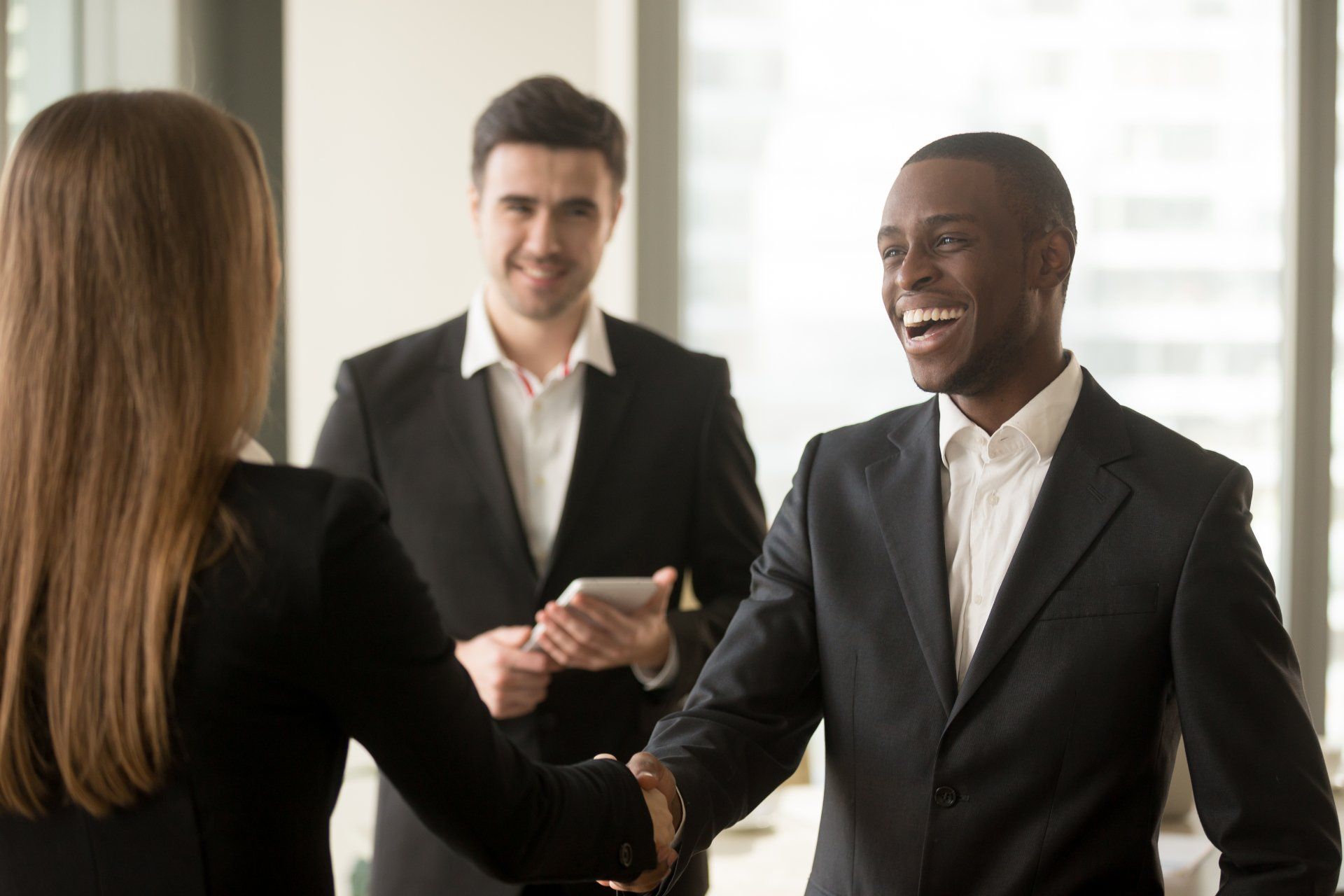 A man and a woman are shaking hands in an office.
