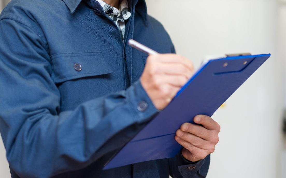 A man in a blue jacket is writing on a clipboard with a pen.