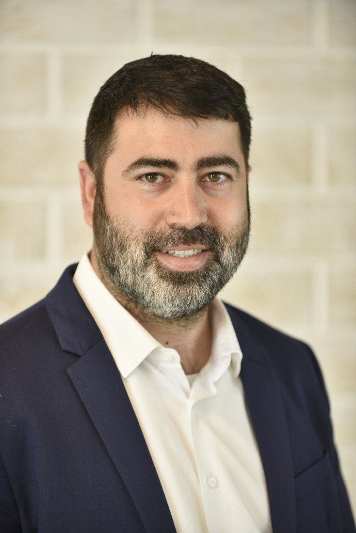 גבר עם זקן לובש חליפה כחולה וחולצה לבנה.