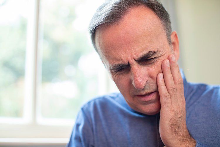 Man with hand on cheek, grimacing, suggesting a toothache.