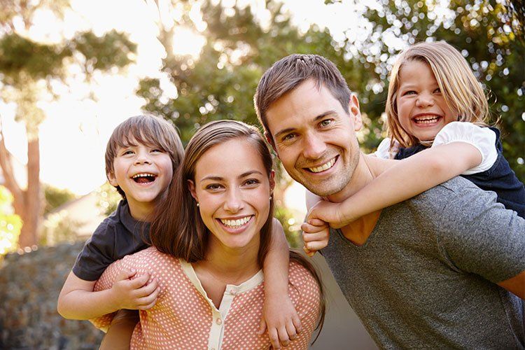 Smiling family of four outdoors: mother, father, and two children, sunny day, piggyback rides.