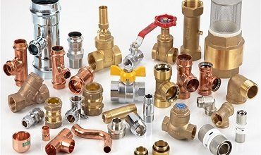 Accesorios de fonaneria variados: tuberías de cobre y latón, válvulas, conectores y otras piezas, expuestas sobre una superficie blanca.