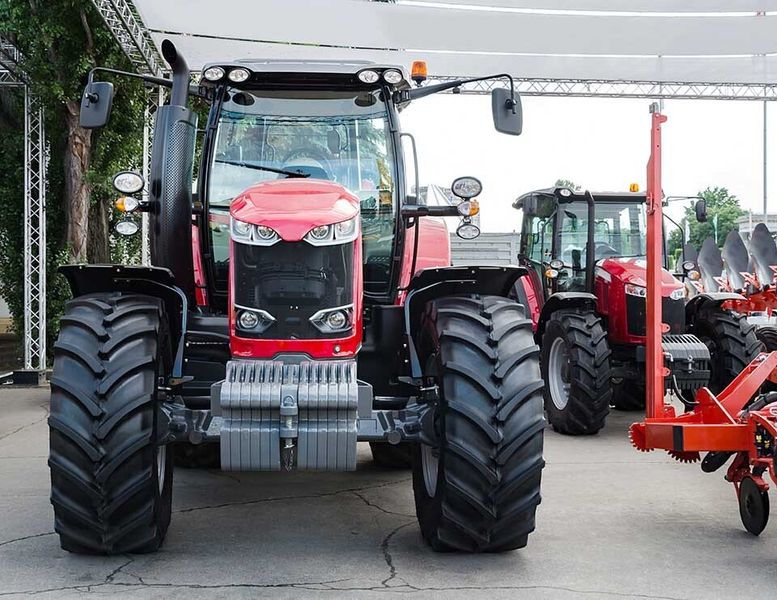 trattore rosso in primo piano con macchine agricole nello sfondo