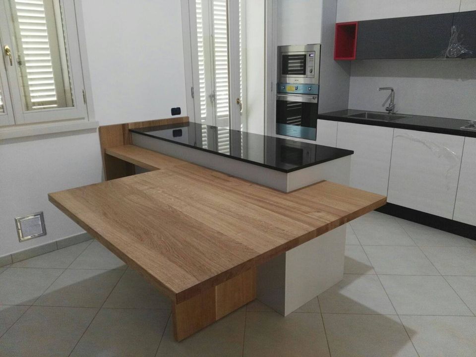 Moderna isola da cucina con piano di lavoro in legno e nero. Mobili bianchi e forno sullo sfondo.