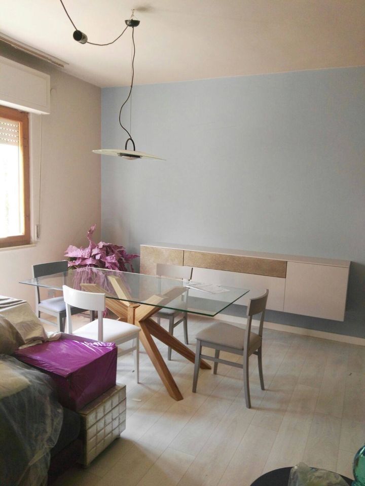 Sala da pranzo con tavolo in vetro, quattro sedie, mobiletto a parete e lampadario a sospensione.