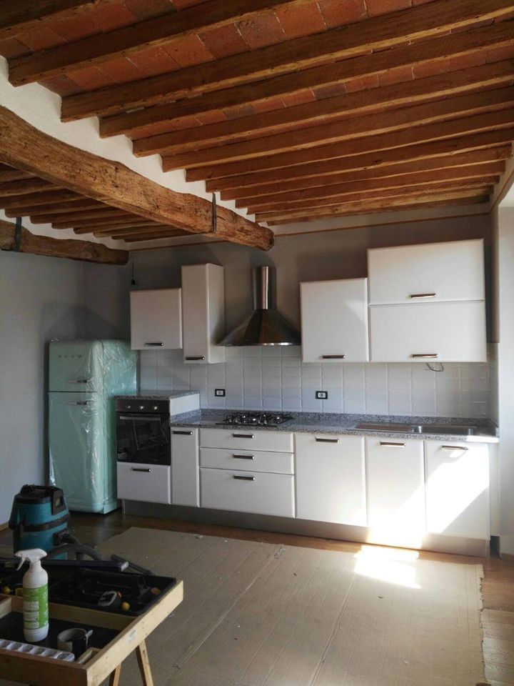 Cucina con mobili bianchi, frigorifero blu, travi in legno al soffitto e cappa in acciaio inossidabile.