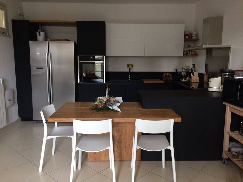 Cucina moderna con mobili bianchi e neri, frigorifero in acciaio inox e tavolo in legno con quattro sedie bianche.