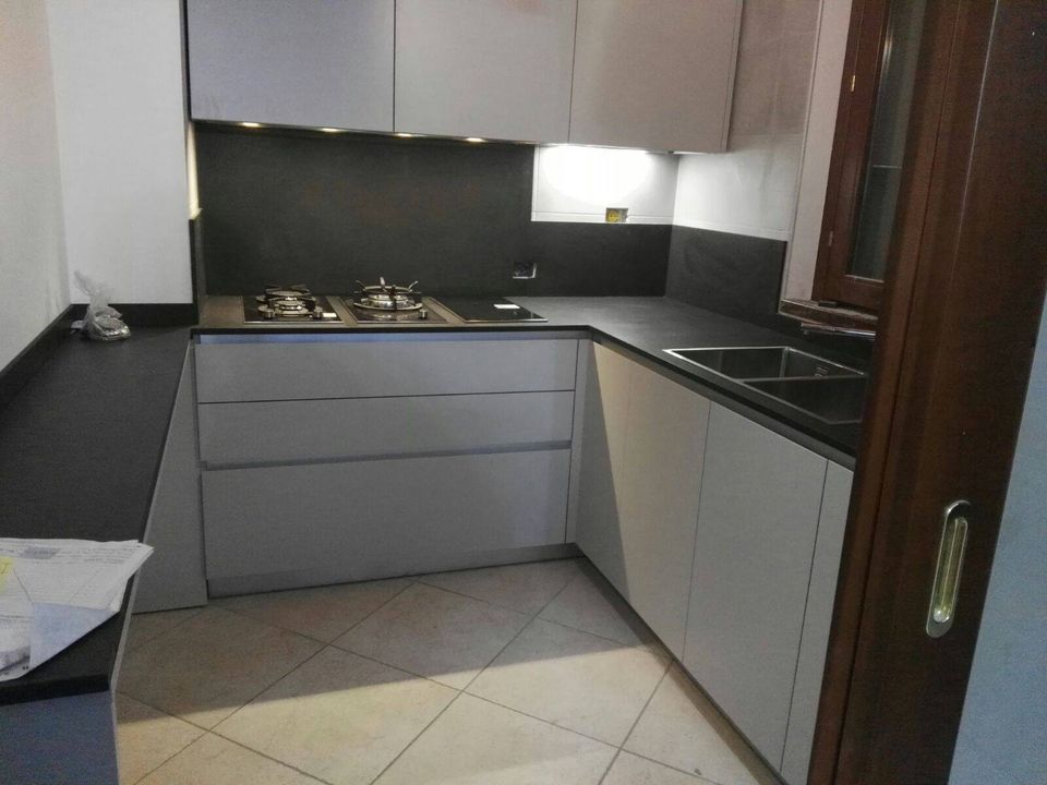 Cucina moderna a L con mobili grigi, ripiani neri e fornello a gas.