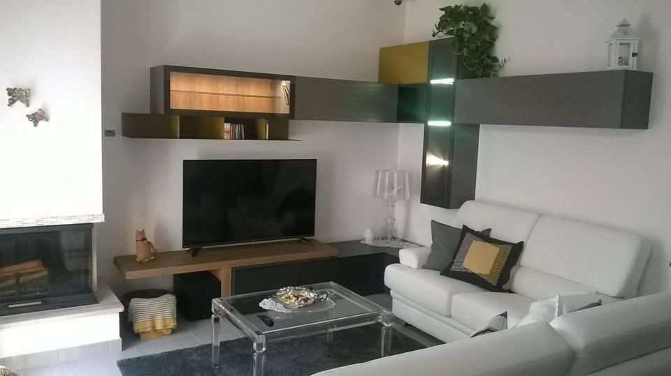 Soggiorno moderno con divano bianco, TV, camino e mensole sospese.